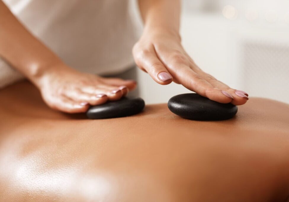 Masseur doing back hot stone massage to woman in spa salon, closeup