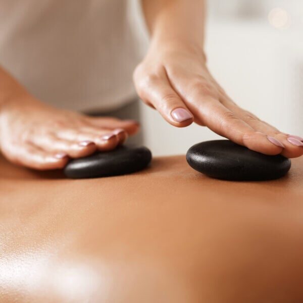 Masseur doing back hot stone massage to woman in spa salon, closeup